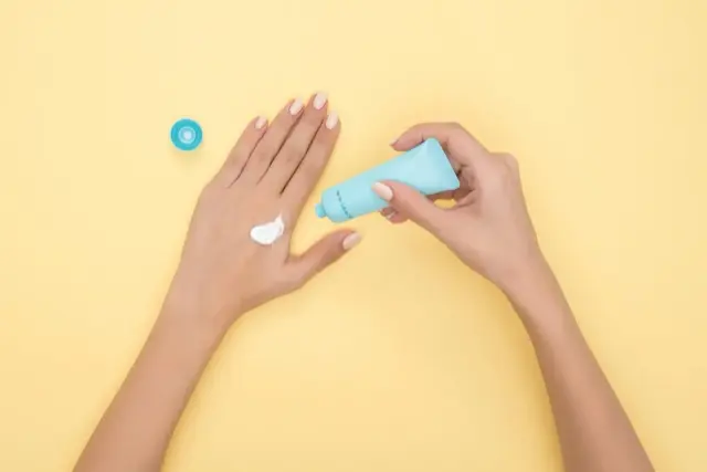 Top-down view of a hand with a dab of white cream, the other hand holding a blue tube