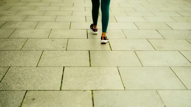 Person in green leggings and trainers walking away along a paved stone pavement