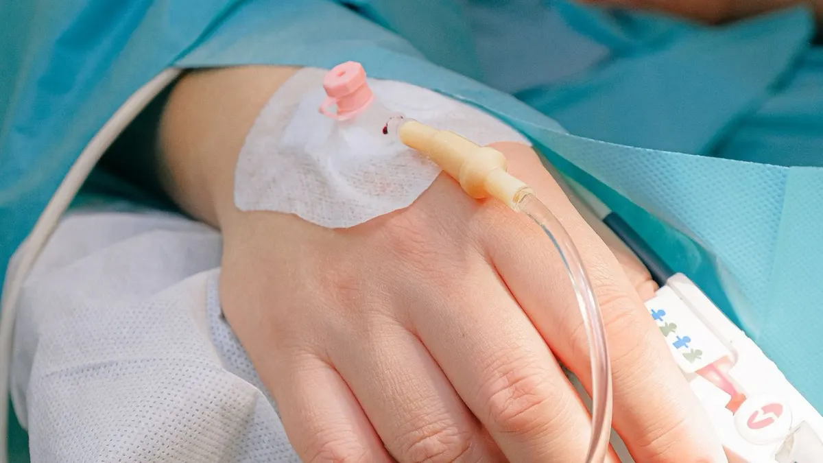 Close-up of a hand with an intravenous cannula taped in place and a clear tube leading away