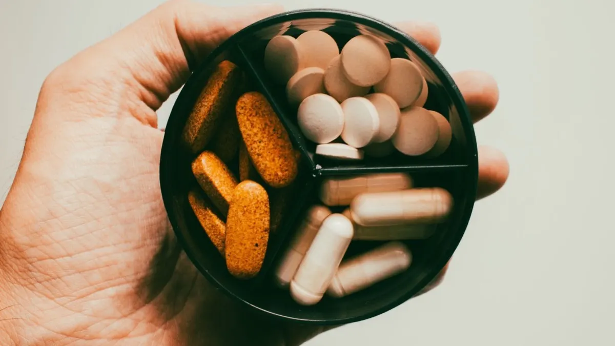 Hand holding a round pill organiser filled with assorted tablets and capsules, no packaging or labels visible