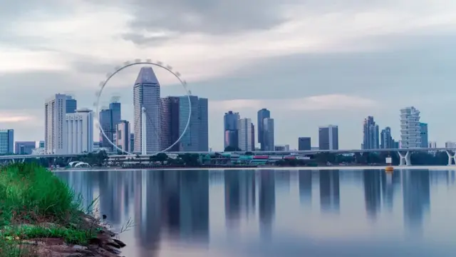 Singapore city skyline and the Singapore Flyer observation wheel reflected in calm water under a cloudy sky